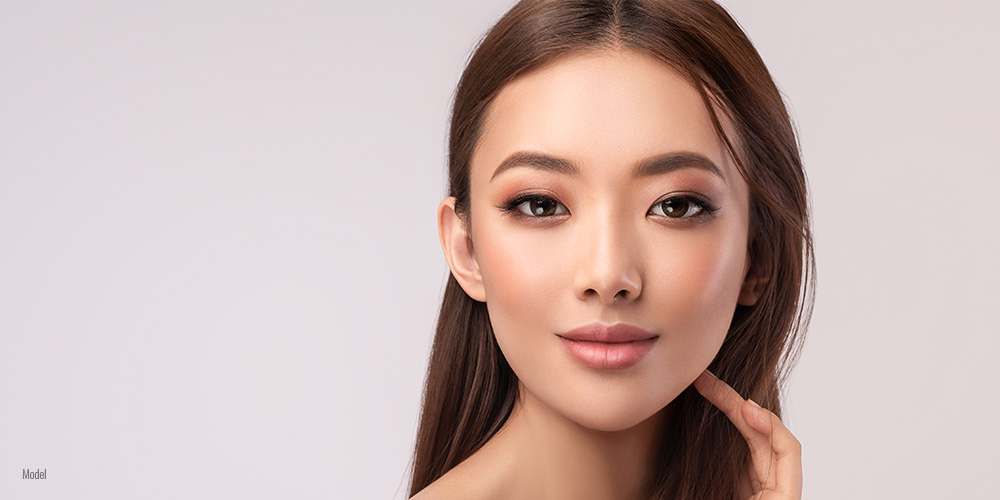 A beautiful, young, bare-shouldered Asian woman looks directly into the camera while being photographed.