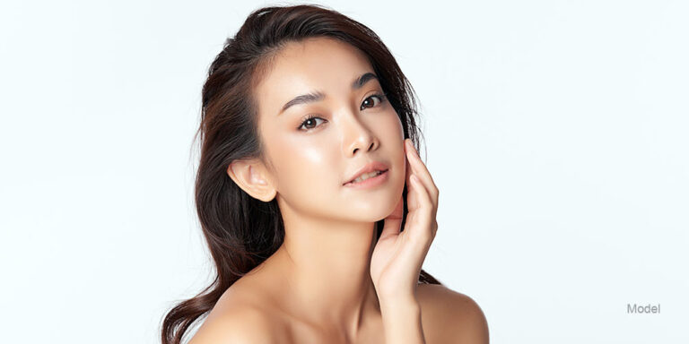 Pretty Asian woman pictured against white background touching her cheek.