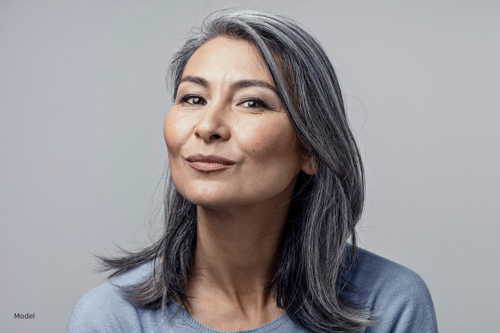 Mature Asian woman with salt-and-pepper hair, light gray background